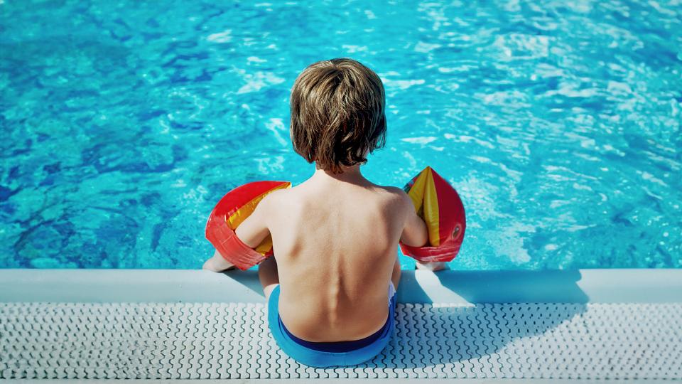 young boy sitting by side of swimming pool